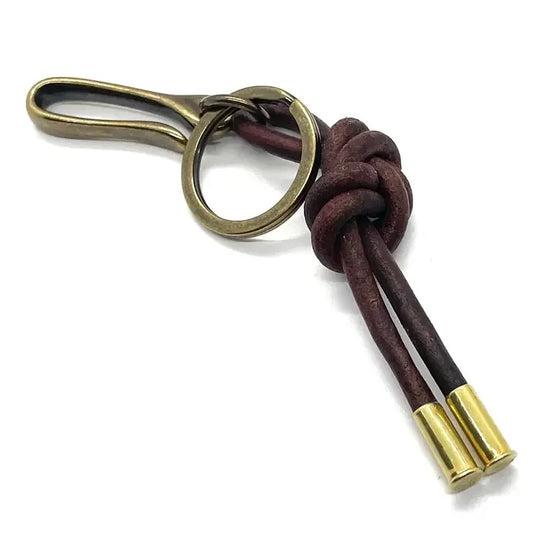 The Oncho Keychain by Tres Cuervos features a brass round keyring, a hook, and two dark leather cords in a figure 8 knot, each finished with a sleek brass cap.