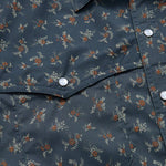 Close-up of the Howler Brothers Open Country Tech Shirt in Rancher Floral, featuring a dark blue small floral pattern, pearl snap buttons, a pointed flap pocket, and UPF 35 sun protection.