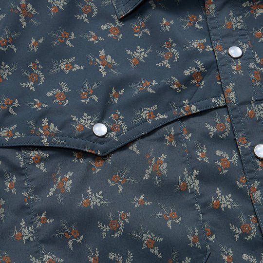 Close-up of the Howler Brothers Open Country Tech Shirt in Rancher Floral, featuring a dark blue small floral pattern, pearl snap buttons, a pointed flap pocket, and UPF 35 sun protection.