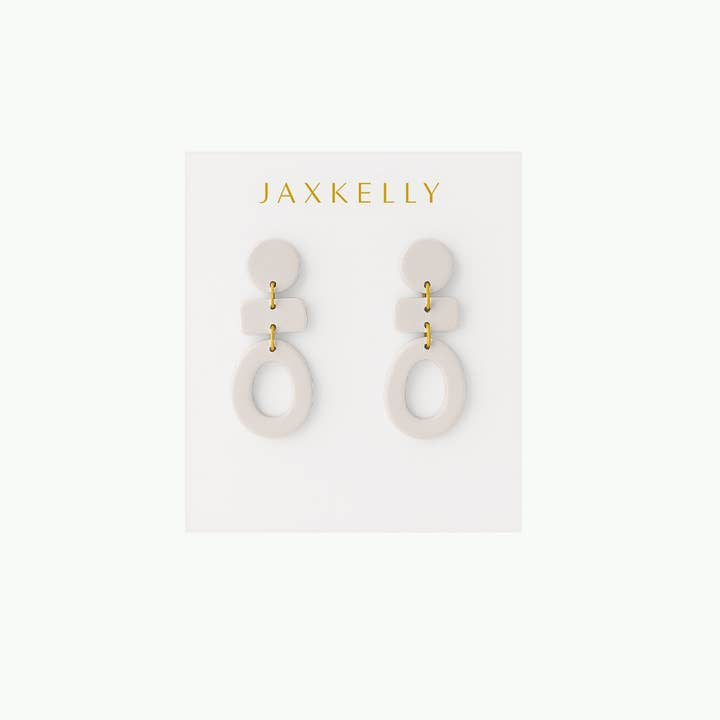 The Organic Three Tier Clay Earring in Oat Milk by JaxKelly features off-white, handcrafted geometric drops of lightweight polymer clay, displayed on a branded white JaxKelly card with gold lettering.