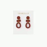 The Organic Three Tier Clay Earring - Terracotta by JaxKelly features geometric, rust-toned tiers with gold connectors. Lightweight and stylish, these earrings add a modern touch to any outfit. Displayed on a white "JaxKelly" card.