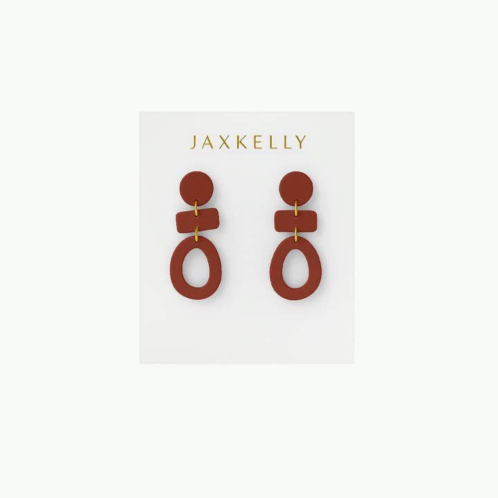 The Organic Three Tier Clay Earring - Terracotta by JaxKelly features geometric, rust-toned tiers with gold connectors. Lightweight and stylish, these earrings add a modern touch to any outfit. Displayed on a white "JaxKelly" card.