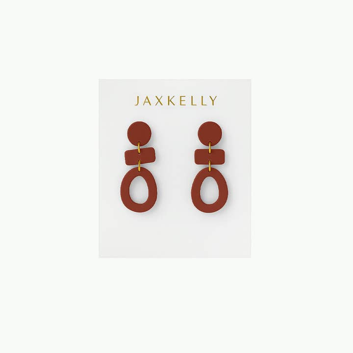 The Organic Three Tier Clay Earring - Terracotta by JaxKelly features handcrafted geometric shapes in rust tones. Lightweight and eye-catching, the earrings are displayed on a white "JaxKelly" card.