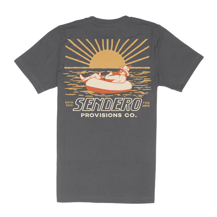 The Out Yonder T-Shirt by Sendero Provisions Co. is a dark gray, soft organic cotton tee with a sunset graphic of a person in an inner tube and "Sendero Provisions Co. ESTD 2014 TRD MRK." text.