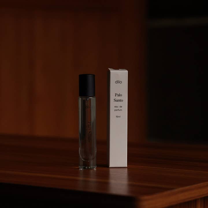 A clear glass bottle with a black cap stands beside a white box labeled "Palo Santo Eau De Parfum | dilo" by dilo, set on a wooden surface, capturing the rich warmth of Palo Santo fragrance.