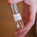 A hand holds a small glass bottle of "Parfum | Rita’s Car" by Saint Rita Parlor, with a silver cap and white label, containing a unisex fragrance made from organic essential oils.