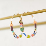 The Pastel Beaded Hoops by Jill Makes feature large 45mm gold-filled hoops adorned with colorful beads in assorted shapes, displayed on a gold rod. Lead and nickel free for comfortable wear.
