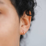 Close-up of a person's ear wearing JaxKelly's Pave Spiral - Gold Earrings: one plain gold hoop and one with small clear stones, both hypoallergenic, shown against a blurred background.