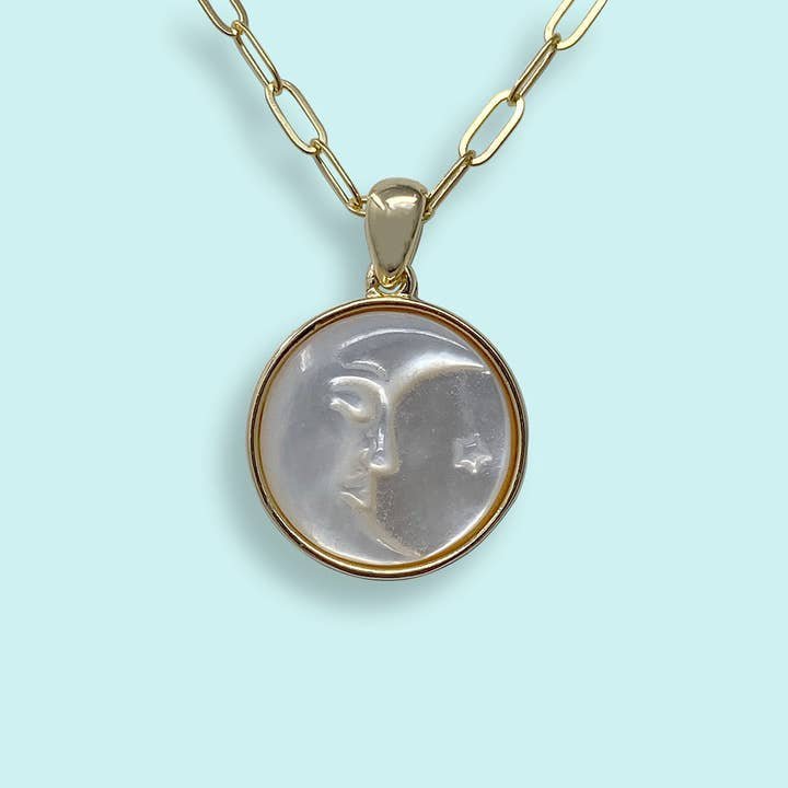 The Pearl Man-in-the-Moon Necklace by Ornamental Things features a gold chain and a round mother-of-pearl pendant with an embossed crescent moon, profile face, and star on a light blue background.