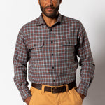A man wears the Duck Head Performance Flannel Sport Shirt, a long-sleeve, button-up plaid shirt in brown and blue with moisture-wicking fabric, tucked into tan pants and paired with a dark brown belt.