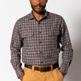 A man wearing a Duck Head Performance Flannel Sport Shirt in brown and blue plaid with chest pockets and tan pants stands against a plain white background.
