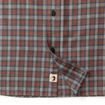 Close-up of the Duck Head Performance Flannel Sport Shirt in red, blue, and grey plaid with black buttons and a square bird logo patch near the hem. Made from moisture-wicking flannel for all-day comfort.