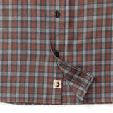 Close-up of the Duck Head Performance Flannel Sport Shirt, a brown, blue, and gray plaid moisture-wicking shirt with black buttons and a logo tag on the hem—ideal for outdoor hiking.