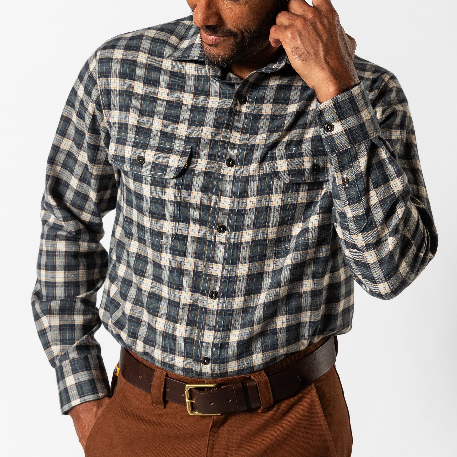 A man wears the Duck Head Performance Flannel Sport Shirt, a blue and gray plaid wool-polyester button-up with chest pockets, paired with brown pants, standing against a plain white background.