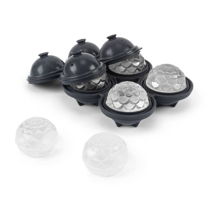 The W&P Petal Ice Mold is shown on a white background, with spherical, textured cocktail ice balls inside and beside the black silicone molds.