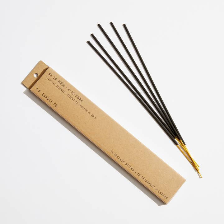 Four hand-dipped Pinon Incense Sticks by P.F Candle with gold bases rest beside a brown “P.F. Candle Co.” box, ready to infuse your space with the calming scent of piñon cedar vanilla.