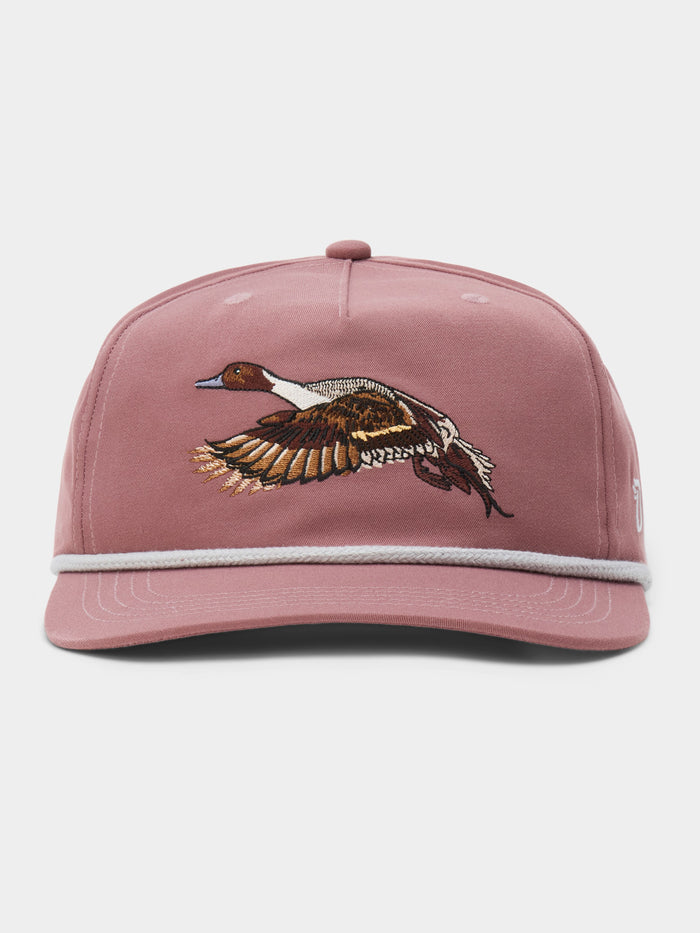 The Pintail Hat by Duck Camp is pink with white trim and features an embroidered flying duck (bull sprig) on the front.