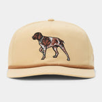 Introducing the Duck Camp Pointer Hat by Duck Camp—a tan baseball cap featuring an embroidered brown and white pointer dog on the front panel and a stylish brown rope detail along the brim. This adjustable cap offers both comfort and style, making it ideal for everyday wear.