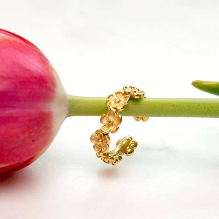 The Posy Ring - 18K Gold Plated by Peter and June, a waterproof floral ring, is shown on a pink tulip stem against a white background.