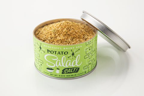 A round can with a green label reading "Potato Salad Salt | Beautiful Briny Sea" by Beautiful Briny Sea, filled with a yellowish seasoning blend perfect for grilled veggies or your favorite dishes.