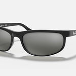 The Ray-Ban 2027 Predator 2 sunglasses feature a black curved frame, dark tinted lenses, and sporty Predator temple tips, creating an athletic look against a plain, light background.