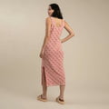 A woman faces away, wearing the Sendero Provisions Co. Puebla Knit Dress | Sendero in pink with a sleeveless design, crocheted details, side slit, and beige sandals, set against a plain beige background.
