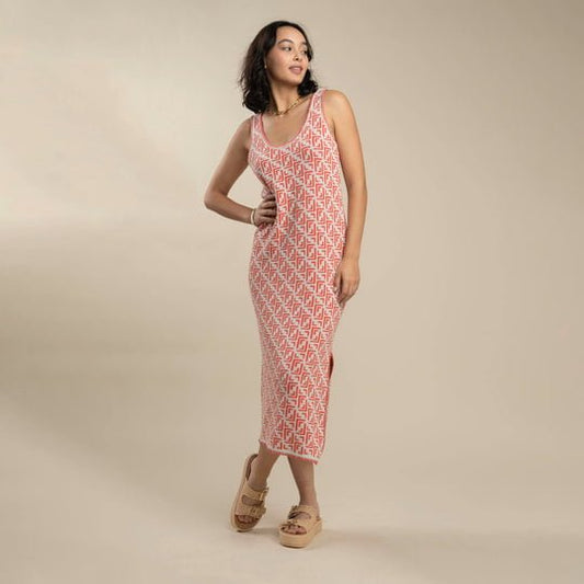 A woman stands on a neutral background wearing the Sendero Provisions Co. Puebla Knit Dress, a sleeveless, ankle-length dress with a red and white pattern, styled with beige platform sandals.