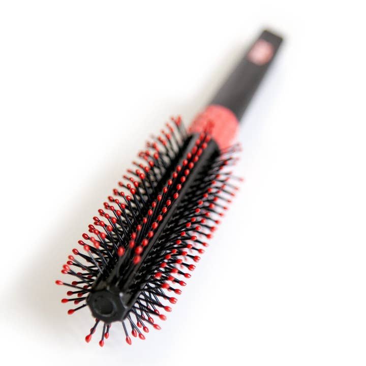 The Uppercut Deluxe Quiff Roller is a black, round hair styling brush with red-tipped bristles, perfect for creating a pompadour, shown on a white background.