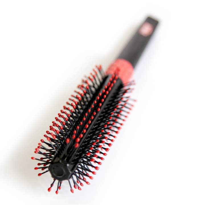 The Uppercut Deluxe Quiff Roller, a black hair styling brush with red-tipped bristles, rests on a white surface—ideal for creating a sharp pompadour.
