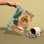 A hand holds a colorful Rainy Day 1,000 Pieces puzzle box by Birdie Puzzles, featuring an illustrated design, next to a tipped-over cup spilling recycled puzzle pieces onto a flat surface.