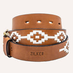 The Rambler belt by Zilker Belts is crafted from Argentine leather with white geometric stitching, a brass buckle, and "ZILKER" embossed near the end for unique detail.