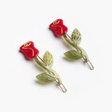 The Winona Irene Red Rose Acetate Barrette Hair Clip Set features two cellulose acetate clips shaped like red roses with green stems and leaves, shown on a white background.