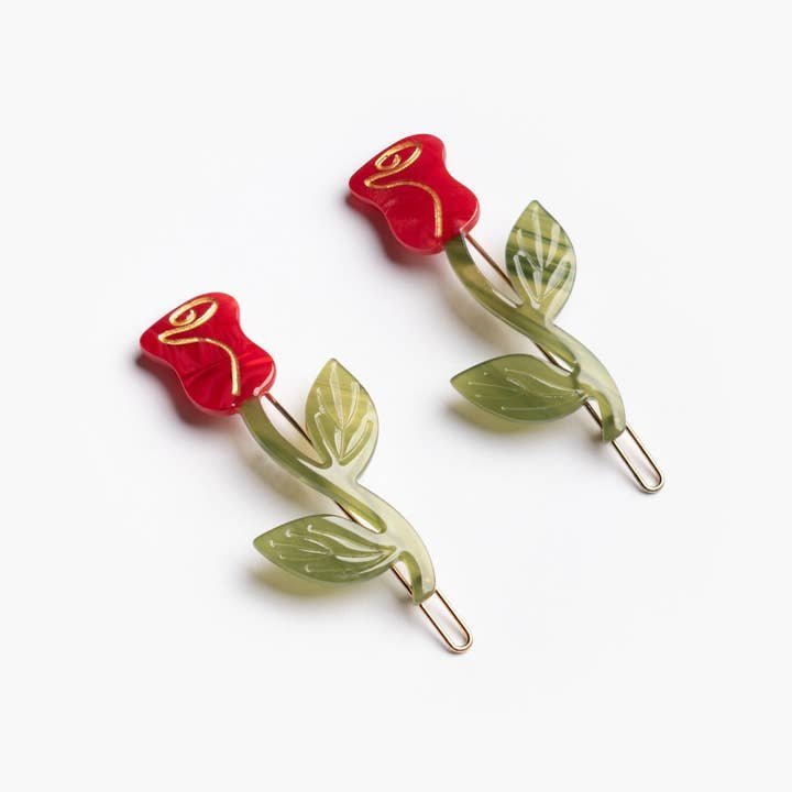 The Winona Irene Red Rose Acetate Barrette Hair Clip Set features two cellulose acetate clips shaped like red roses with green stems and leaves, shown on a white background.