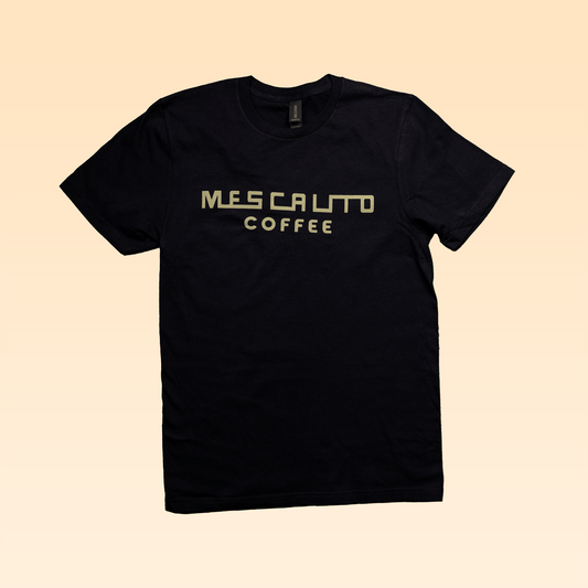 The Retro Mescalito Marzocco t-shirt by Mescalito Coffee features "MESCALITO COFFEE" in light yellow block letters and a retro La Marzocco emblem on black, shown against a beige background.