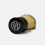 The Rockwell Synthetic Shaving Brush by Rockwell Razors features beige bristles and a black handle with a white logo, lying on its side, designed for classic razor shaving.