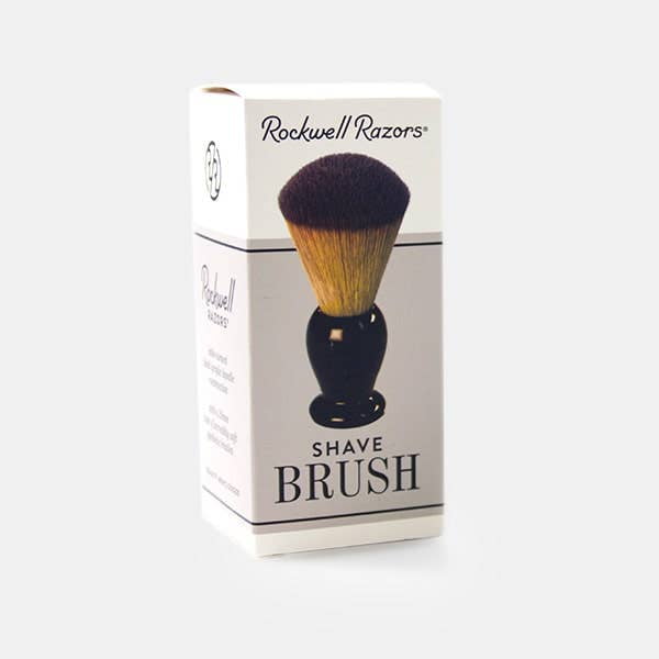 A box of the Rockwell Synthetic Shaving Brush by Rockwell Razors, featuring brush imagery and black branding, emphasizes soft bristles for a comfortable shave.