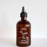 A brown glass spray bottle labeled "Room & Linen Spray | Gut Feeling | Ballad of the Bird Dog" by Ballad of the Bird Dog, with a black plastic pump, filled with essential oils, stands on a white surface against a plain background.
