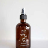 A brown glass spray bottle labeled "Room & Linen Spray | Tattoo Ink | Ballad of the Bird Dog" by Ballad of the Bird Dog, with a black cap, sits on a white surface against a plain background.