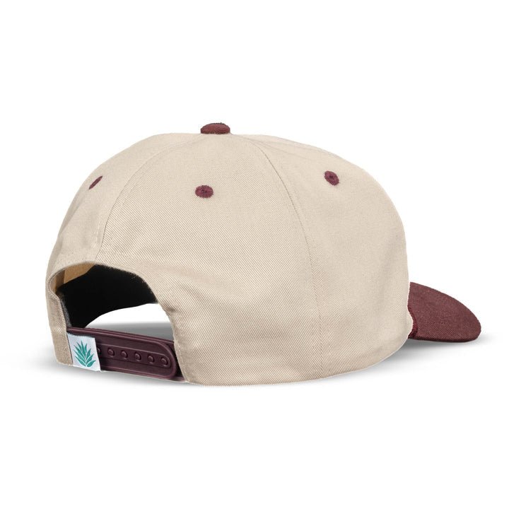 The Sendero Provisions Co. Roping Champ Hat is a beige and maroon 5-panel cap with an adjustable snapback, a small woven label featuring a green plant graphic, and durable twill construction for everyday comfort.