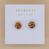 Round CZ Coffee Gold Earrings by JaxKelly: faceted amber-colored studs on a white card with gold text. Hypoallergenic, gold-plated for comfort and lasting shine.