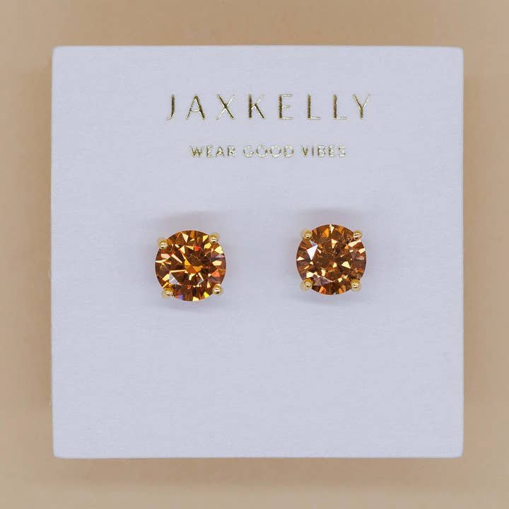 Round CZ Coffee Gold Earrings by JaxKelly: faceted amber-colored studs on a white card with gold text. Hypoallergenic, gold-plated for comfort and lasting shine.