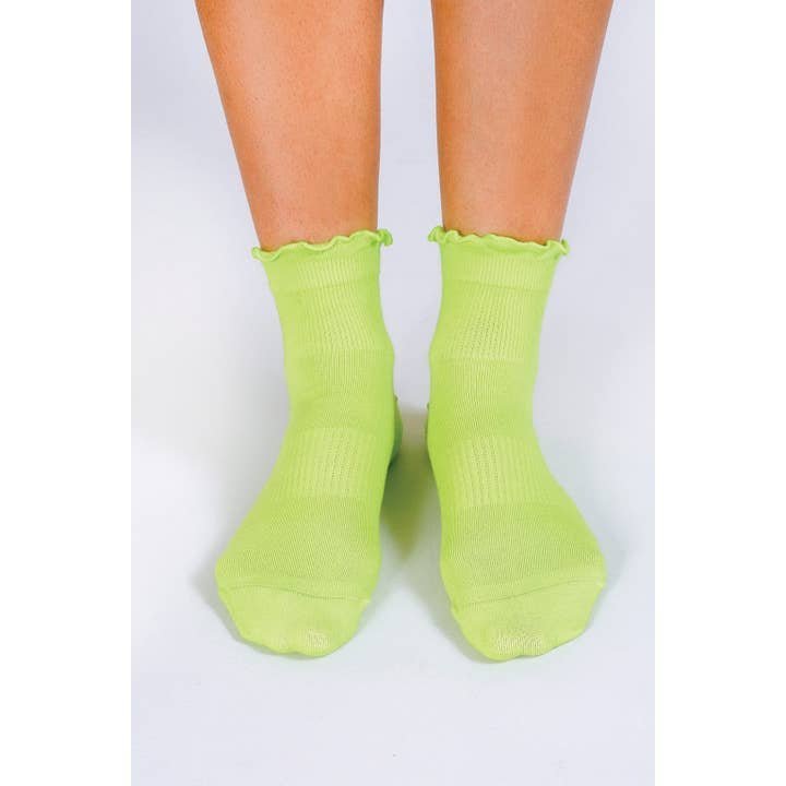 A person wears Tailored Union's Ruffle Ankle Sock in light green with reinforced heel, standing on a white surface.