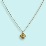 The Sacred Heart Necklace by Ornamental Things features a gold-plated sunburst design with a heart at the center, vintage-inspired pendant, and is pictured on a light blue background.