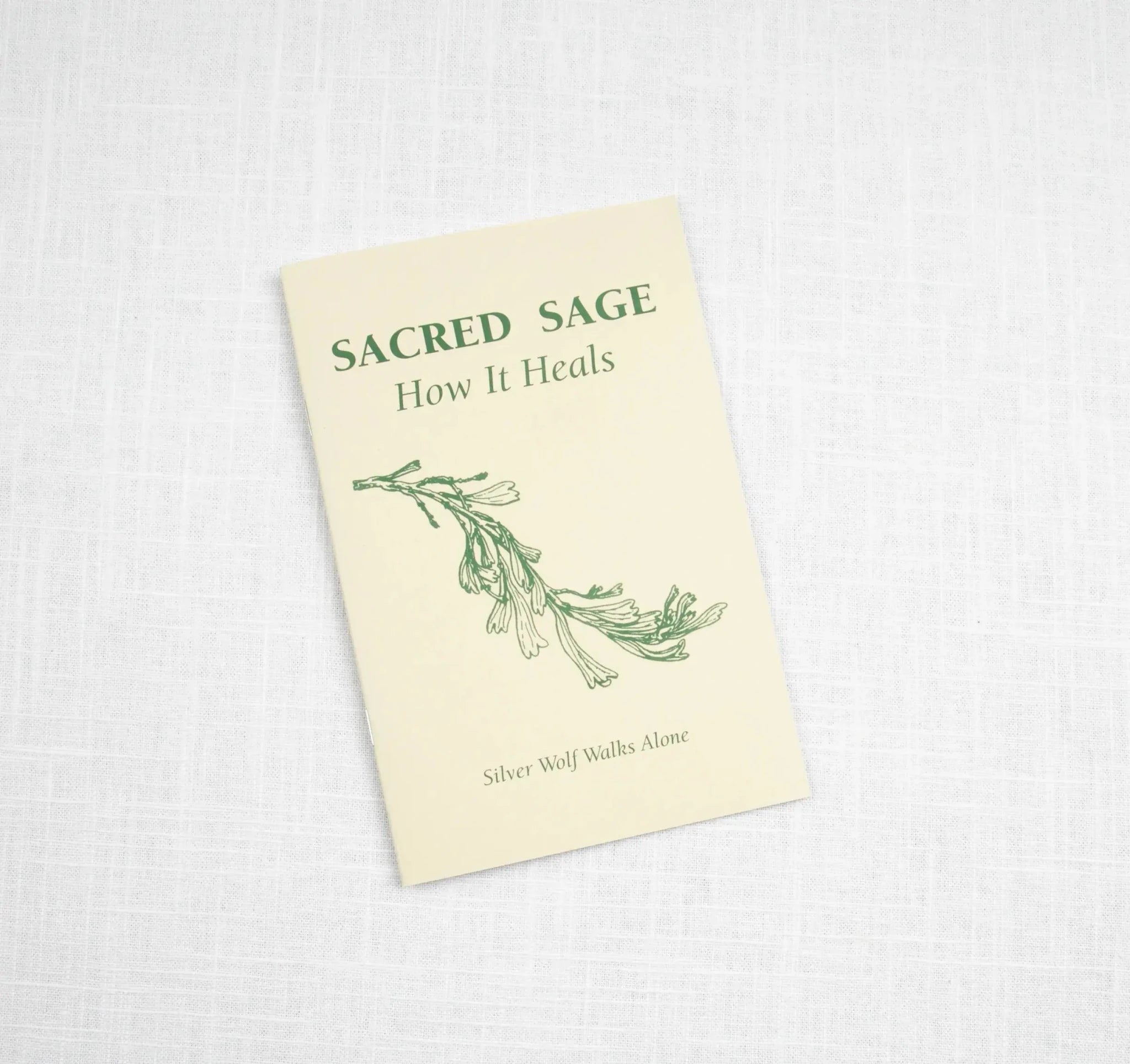 The Sacred Sage by Taos Herb Co. features a green sage design on a cream cover and explores healing with sage, displayed on a white textured surface.