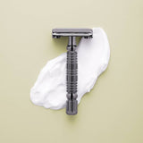 The Rockwell Razors Safety Razor | R1 is shown on a light surface with a smear of shaving cream, highlighting this plastic-free razor designed for a smooth shave.