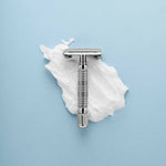The Rockwell Razors Safety Razor | R1 rests on shaving cream against a light blue background, showcasing the smooth shave and plastic-free experience offered by Rockwell Razors.