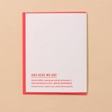 A white letterpress Sardine Love Card by And Here We Are, featuring a red border and orange “AND HERE WE ARE” text, is shown on a beige surface.