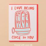 The Sardine Love Card by And Here We Are features sardines in a tin with "I love being close to you" in red and orange neon ink—a quirky love card for someone special.