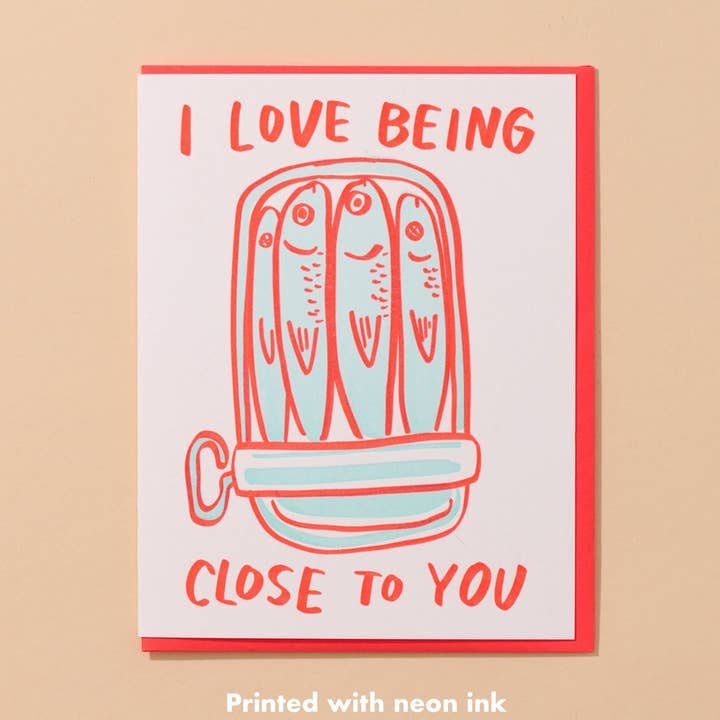 The Sardine Love Card by And Here We Are features sardines in a tin with "I love being close to you" in red and orange neon ink—a quirky love card for someone special.
