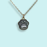 The Shell Paw Print Necklace by Ornamental Things, featuring a paw print-shaped pendant, is displayed against a light blue background.